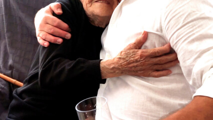 An elderly hundred-year-old man, grandmother, tightly hugs a middle-aged man with wrinkled arms....