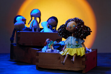 Textile handmade doll with blue-yellow dress sits on a wooden box with colorful fabric scraps