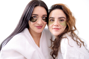 Two young female friends clients of beauty salon in white coats, chating between spa procedures