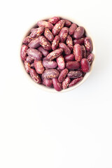 Uncooked, variegated kidney bean seeds in bowl on white background. Top view. Space for a text
