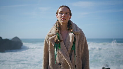Fashion girl posing ocean in coat portrait. Attractive lady with braids at shore