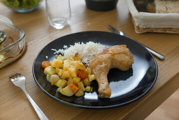 A well-prepared dinner of roasted chicken, rice, and vegetables on a green plate, set on a wooden...