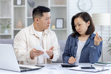 Fototapeta premium Couple having a serious discussion about finances at home, with bills and a laptop on the table. Concern and tension are visible.
