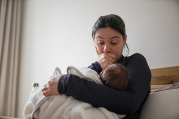 Mother breastfeeding her baby while holding them close, conveying a mixture of exhaustion and...