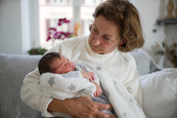 Grandmother in a white sweater holding her newborn grandchild wrapped in a cozy blanket. The tender...