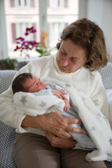 Grandmother gazes lovingly at her newborn grandchild wrapped in a soft, star-patterned blanket. The...