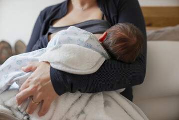 Mother breastfeeding newborn baby while holding them close, creating a strong bond and providing...