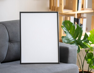 A mockup black framed white picture sits on a gray couch and minimalist background
