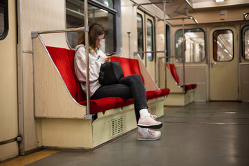 A young woman rides in a modern subway car with a phone in her hands. A beautiful girl in sweater...