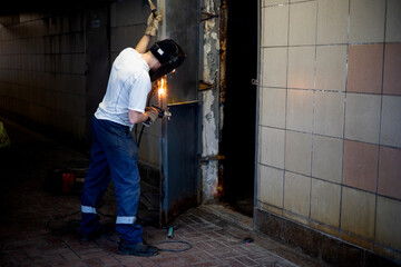 Arc Welding Door Jam. Welder repairing a garage door. Selective focus of welder repairing an iron door.