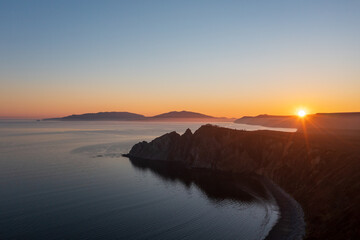Beautiful sunset seascape. Aerial view of rocky cape and sea bay. Evening sun over the coast....