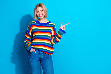 Portrait of pretty young girl indicate finger empty space ad wear striped pullover isolated on blue...