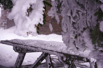 a snowy bench with snow falling off it's sides