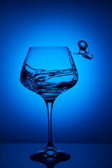 Clear glass containing a dark-blue liquid atop a table, illuminated by a blue light