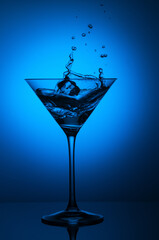 Clear glass containing a dark-blue liquid atop a table, illuminated by a blue light