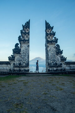 Silhouette of a person standing between two traditional Balinese split gates at dusk with a mountain in the background