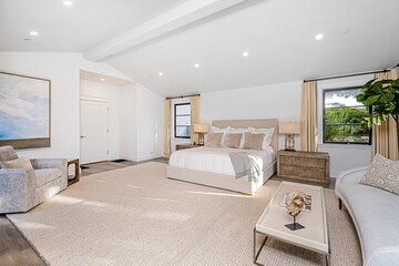 Luxurious master bedroom suite features sumptuous carpeted flooring, a lavish bed and armchairs © Wirestock