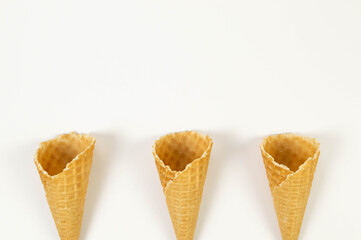 Top view of three ice cream waffle cones on white background. Summer wallpaper, flat lay, copy space.