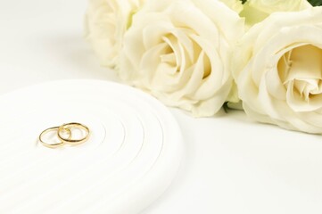 Wedding white roses and gold wedding rings on white background. Wedding composition, white arch tray, podium. Copy space, flat lay.