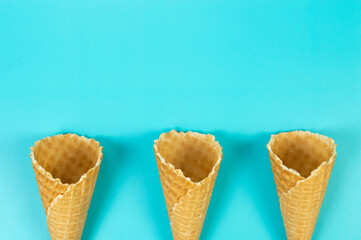 Top view of three ice cream waffle cones on blue background. Summer wallpaper, flat lay, copy space.