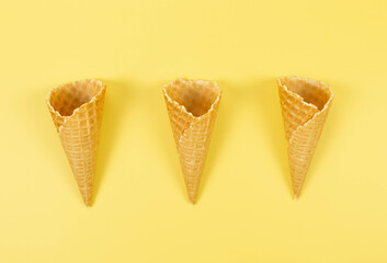 Top view of three ice cream waffle cones on yellow background. Summer wallpaper, flat lay, copy space.