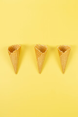 Top view of three ice cream waffle cones on yellow background. Summer wallpaper, flat lay, copy...