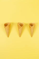 Top view of three ice cream waffle cones on yellow background. Summer wallpaper, flat lay, copy space.