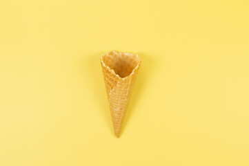 Top view of ice cream waffle cone on yellow background. Summer wallpaper, flat lay, copy space.
