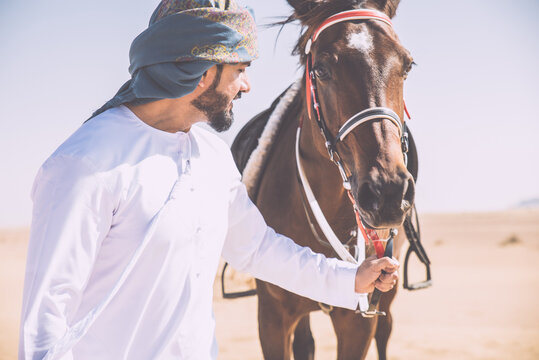 Young adult with Kandura, the emirates traditional clothes, riding his horse in the desert