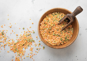 Wooden bowl with scoop of dry raw green and orange peas seeds on light table.Macro.