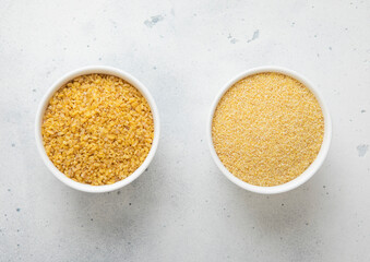 Ceramic bowls with yellow and melted dry bulgur seeds on kitchen table.Macro.