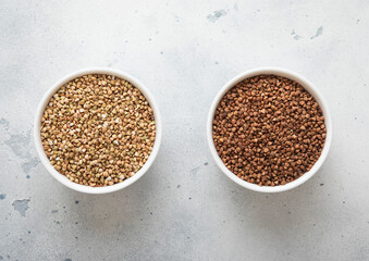 Ceramic bowls with dry raw brown and green buckwheat seeds on kitchen table.Macro.