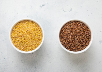 Ceramic bowls with brown and yellow bulgur dry raw seeds on kitchen table.Macro.