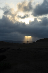 A solitary figure stands under a dramatic sky as sunlight bursts through the clouds. © Marcel