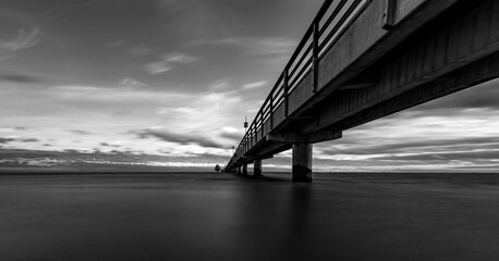 A grayscale shot of the pier with a cloudy sky