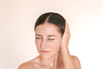 Young caucasian brunette woman is experiencing acute pain in her ear. She presses her ear with her...