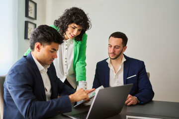 two men and a woman are sitting around a table with a laptop open