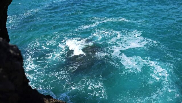 High angle shot of a rocky cliff, with waves crashing in slow motion. Travel, nature and wallpaper concept.