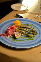 Gourmet fish dish with asparagus, prosciutto, and corn served on a blue plate, perfect for culinary and restaurant promotions with copy space.