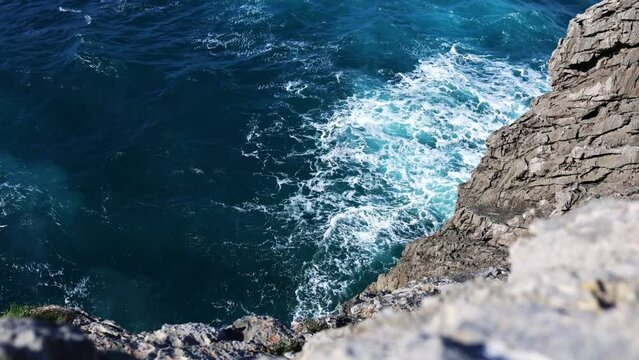 High angle shot of a rocky cliff, with waves crashing in slow motion. Travel, nature and wallpaper concept.