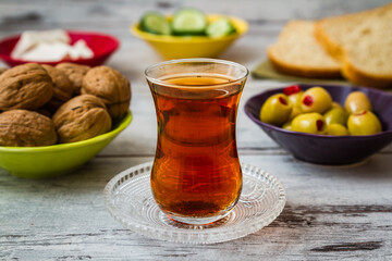 Glass of tea on a saucer, with bowls of cucumbers and bread in the background on a white wooden table.