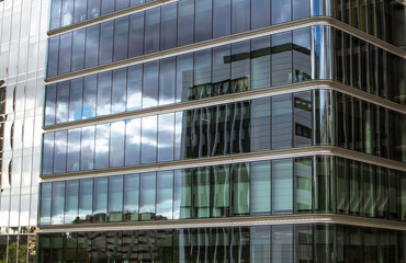 Glass facade of a modern tall office business building with clouds and buildings reflecting. Blue sky reflection. Skyscraper in an urban space.