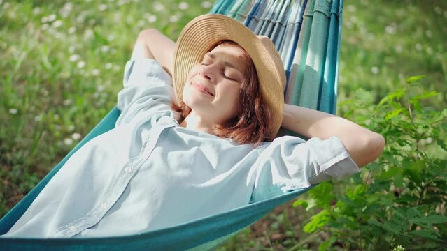 A young Caucasian woman in a hat chilling in a hammock in the spring garden