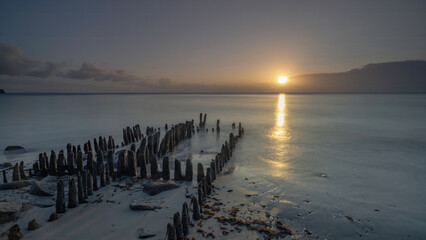 Obraz premium Scenic view of wooden pillars on the beach against the sea at sunset