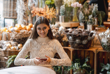 A captivating, colorful girl admiring Christmas decor and browsing her smartphone.