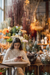 An elegant, bright girl browsing through Christmas decor while using her smartphone.