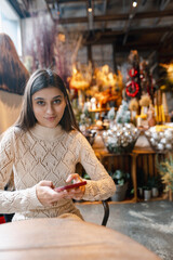 A stunning, colorful young woman browsing Christmas decorations with her smartphone.