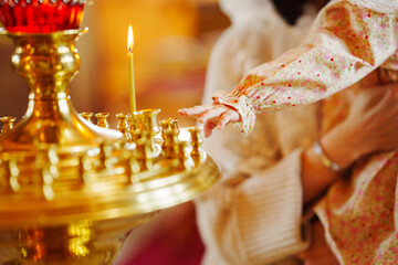 A small child's hand reaches for a candle in a church candlestick. The Sacrament of Baptism of Children in the Orthodox Church. Faith in God.