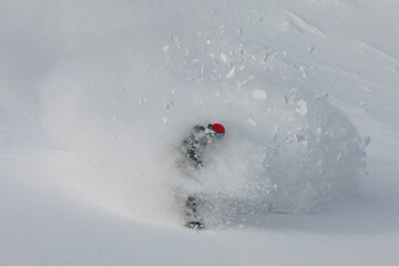 A snowboarder rides out of a cloud of snow breaking in pieces after performing a powder turn on an untouched slope