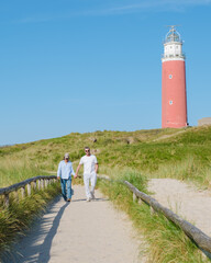 A couple strolling along a path by a stunning lighthouse in Texel, Netherlands, enjoying the scenic...